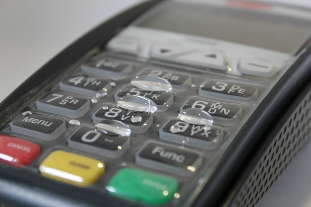 Close-up of waterproof cover on POS terminal keypad with water droplets beading on the surface, demonstrating liquid resistance