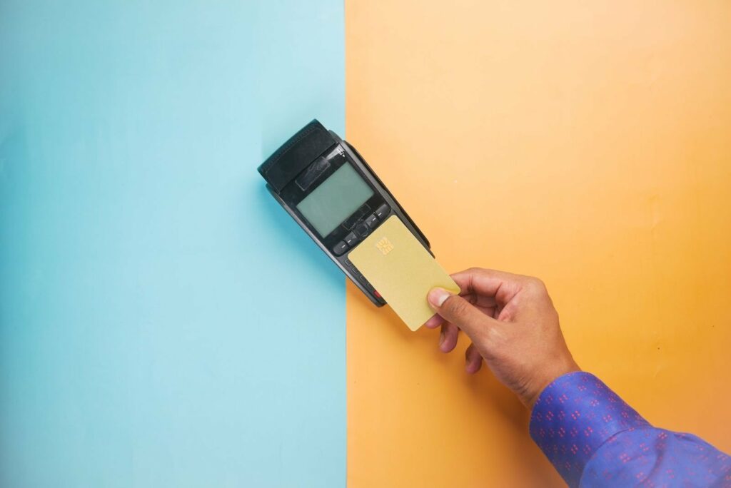 Hand holding a card against a keypad EFTPOS terminal on a two-tone blue and orange background
