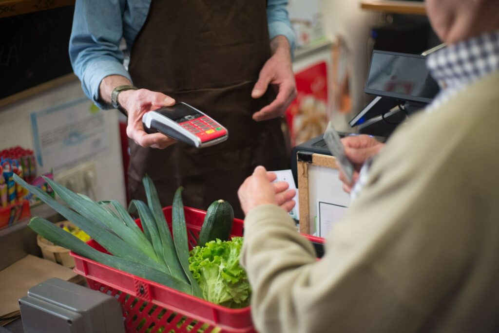 Customer paying by card at a grocery checkout with a basket of vegetables