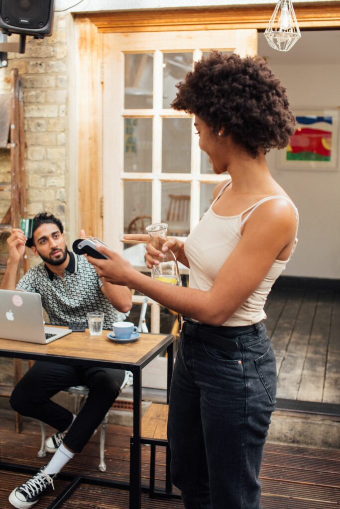 Hospitality staff member holding a portable EFTPOS terminal for a seated customer in a café