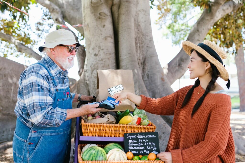 Customer paying by card at an outdoor farmers market stall while the stallholder holds a portable payment terminal