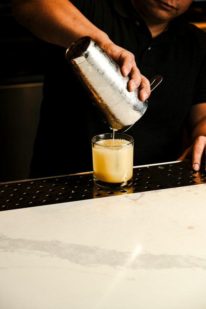 Bartender pouring a cocktail into a glass on a bar counter