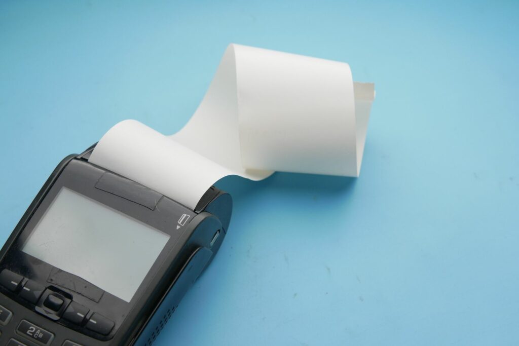 Close-up of a payment terminal screen and keypad with a roll of thermal receipt paper