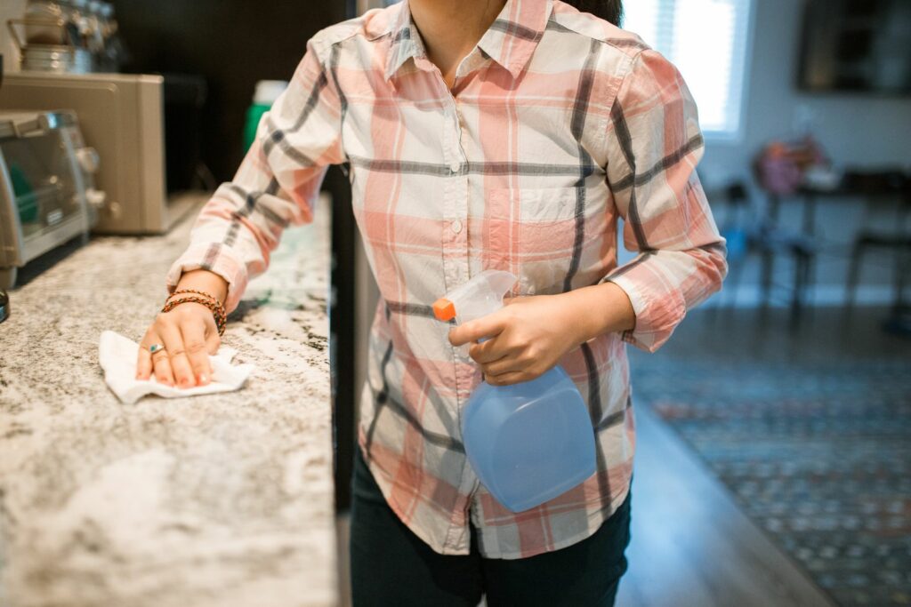 Person using a spray bottle and cloth to wipe down a counter surface