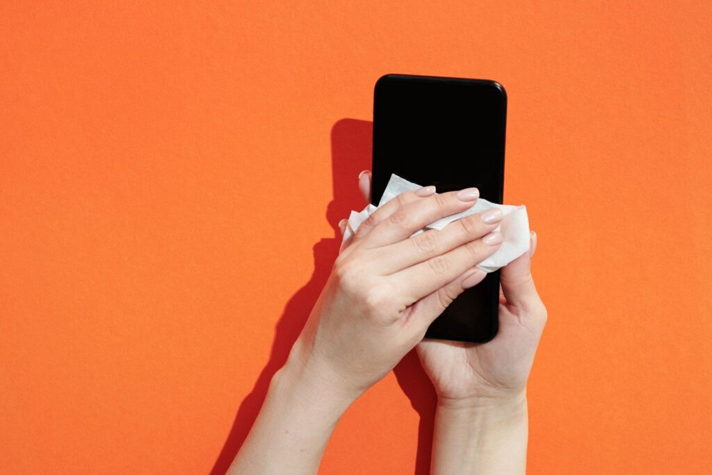 Hands wiping a black touchscreen device with a cloth against an orange background