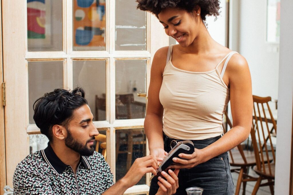Café staff member holding a handheld payment terminal for a seated customer